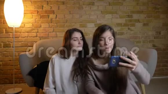 年轻白种人女孩坐在地板上在舒适的家庭氛围中使用智能手机制作自拍照片的肖像视频的预览图