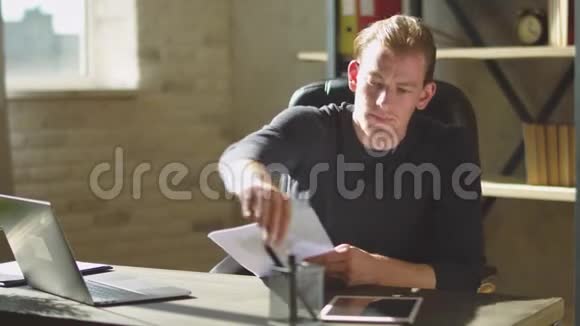 年轻的专心致志的商人坐在办公室笔记本附近的桌子上在文件上工作修改一下视频的预览图