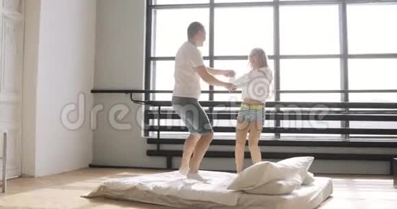 快乐的年轻夫妇在床上跳跃和拥抱双手抱在他们的新公寓里关系概念视频的预览图