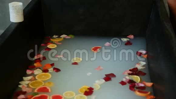女人的手慢慢地在水中混合柑橘片和玫瑰花瓣视频的预览图