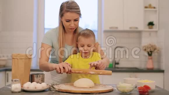 那个漂亮的金发小男孩帮妈妈做饭妈妈和儿子穿着五颜六色的衬衫正在把面团卷出来妈妈是视频的预览图