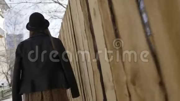 后景一位年轻漂亮的模特女孩戴着宽边帽子和黑色皮夹克在城里散步行动视频的预览图