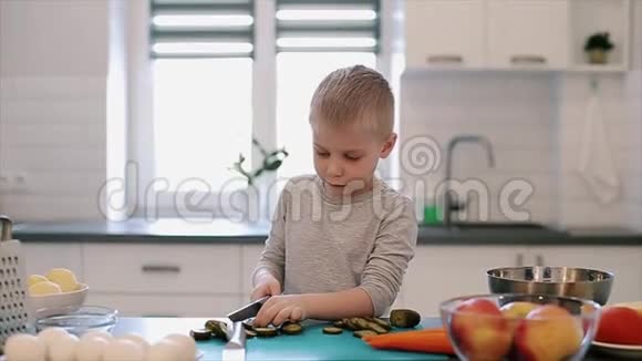 漂亮的白种人小男孩大蓝眼睛在明亮的厨房里做饭视频的预览图