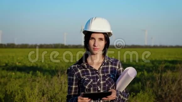 一位戴着建筑头盔和大纸卷的年轻女子站在一片田野里看上去笔直慢动作视频的预览图