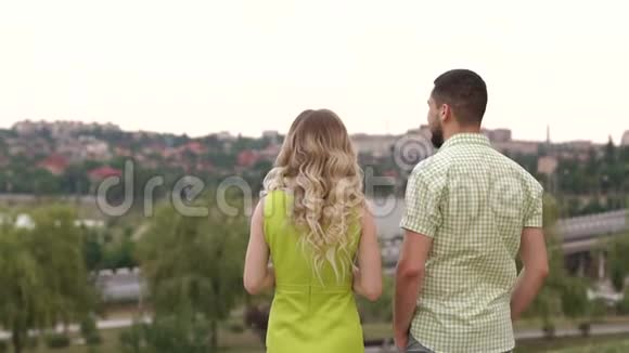 一对相爱的年轻夫妇站在公园里拥抱看着一幅美丽的风景视频的预览图
