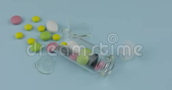 破碎的玻璃瓶上有许多不同的药丸和药物在蓝色背景下旋转视频的预览图