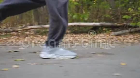 初秋一个运动的男子在森林附近的道路上奔跑年轻运动员的腿沿着小径快速冲刺视频的预览图