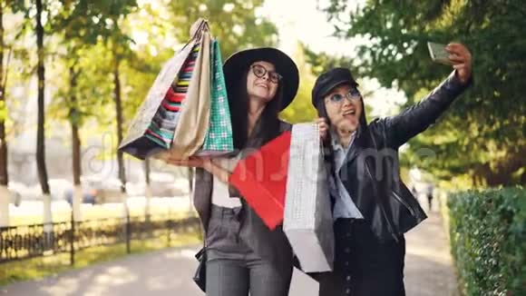 快乐的年轻女性朋友正拿着纸袋在人行道上站在户外摆姿势自拍女孩用的是视频的预览图