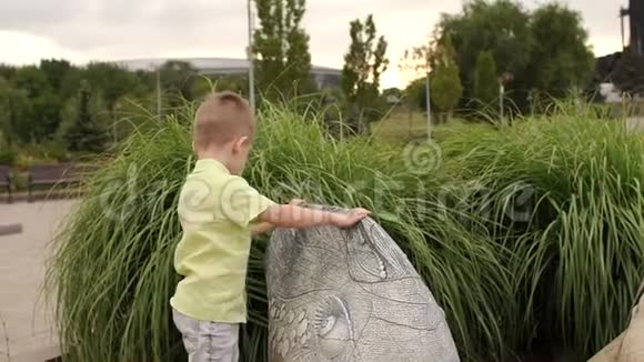 夏天一个小可爱的男孩在操场上玩靠近一座石雕鱼视频的预览图