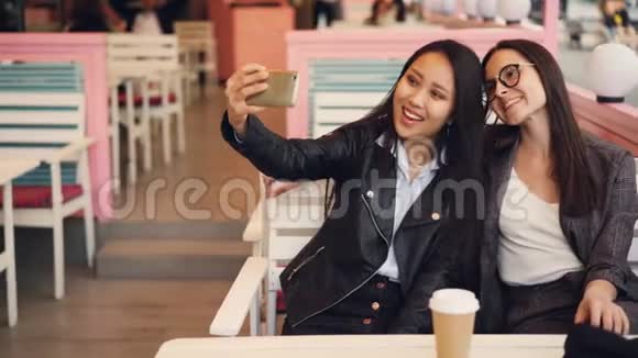 漂亮的亚洲女孩正和她的高加索朋友坐在咖啡馆的桌子上自拍然后看照片淫媒视频的预览图