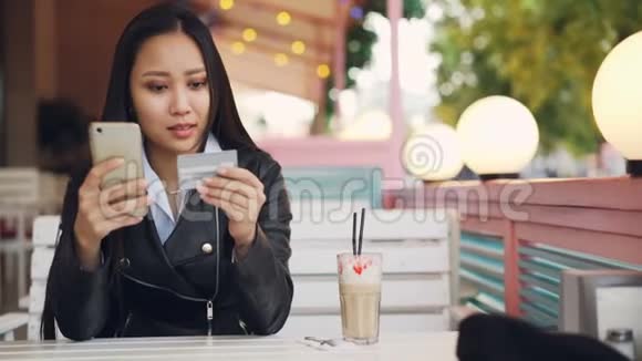 漂亮的亚洲女孩正在使用信用卡和智能手机在露天咖啡馆和视频的预览图