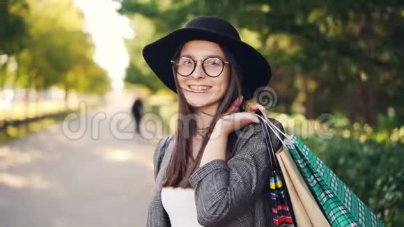 欢快的女购物者拿着纸袋摆姿势看着摄像机微笑着笑着站在街上的画像视频的预览图