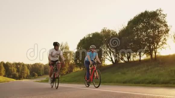 一男一女骑着自行车在日落时分一起慢悠悠地沿着公路行驶这对夫妇骑自行车旅行视频的预览图