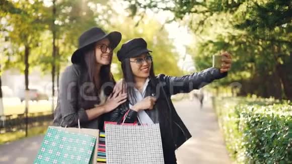 快乐的年轻女性用智能手机在网上打视频电话谈论购物展示购物袋和大笑视频的预览图