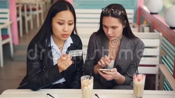快乐的亚洲女孩和高加索女孩正坐在网上商店里用银行卡付款视频的预览图