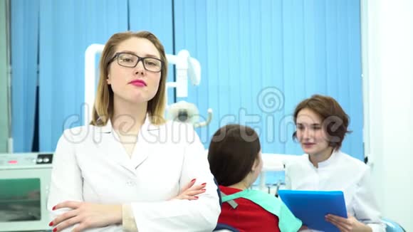 一位身穿白色医用外套的女士站在牙医办公室的摄像头前一位病人和另一位医生正在谈论视频的预览图
