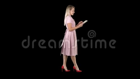 穿着粉色裙子走路的金发美女使用平板电脑阿尔法频道视频的预览图