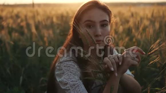 迷人的年轻黑发女孩独自坐在秋天成熟的麦田里视频的预览图