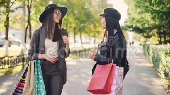 快乐的年轻女性朋友们在街上说着笑着拥抱着拿着纸袋分享新闻视频的预览图
