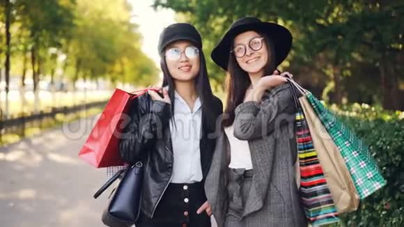 美丽的年轻女性购物者站在街上拿着纸袋微笑着看着相机的画像视频的预览图