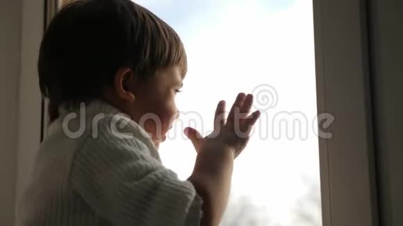 冬天男孩坐在一扇大窗户前挥手视频的预览图