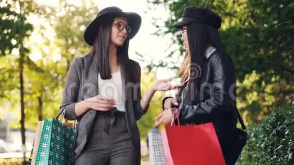 带着购物袋的快乐亚洲女孩正和她站在街上的朋友聊天然后在街上展示她的购物品视频的预览图