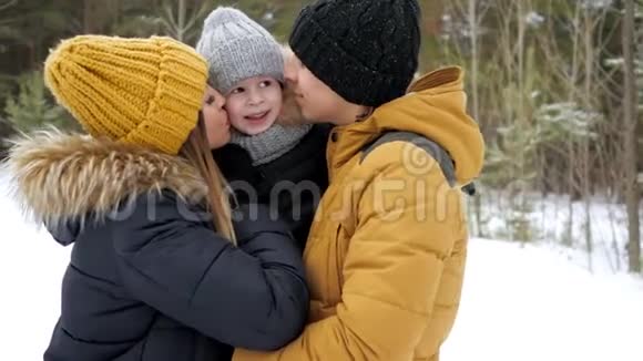 爸爸妈妈在冬天公园拥抱和亲吻他们的小儿子视频的预览图
