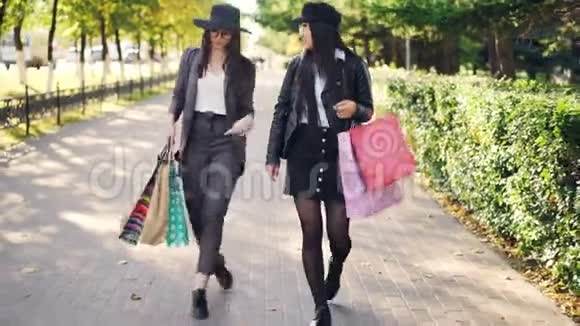 两位迷人的年轻女子从美丽的街道上的商店走出来手里拿着纸袋一边买东西一边说话视频的预览图
