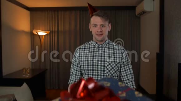 有魅力的男性在舒适的客厅里用大红蝴蝶结领生日礼物盒视频的预览图