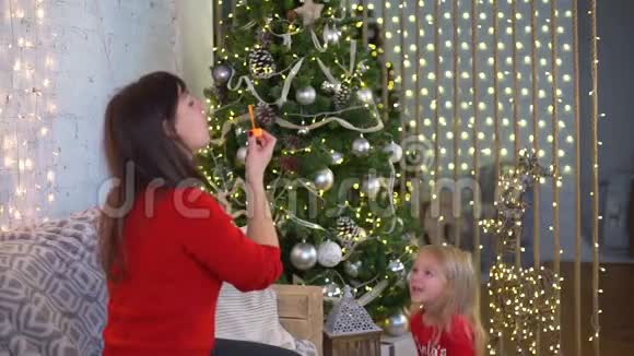 母亲和女儿在圣诞树附近吹泡泡视频的预览图