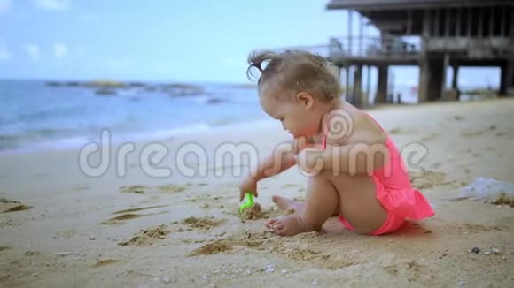 小女孩穿着粉红色的泳衣在蓝色的大海的岸边玩沙子快乐童年的概念时尚视频的预览图