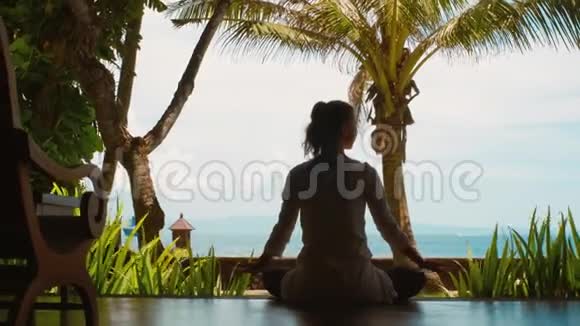 女子剪影正在莲花的位置练习瑜伽冥想双手伸展在海边美丽的景色视频的预览图