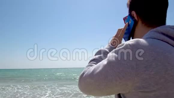 在希腊的哈尔基迪基年轻人看着大海用手机在沙滩上聊天视频的预览图