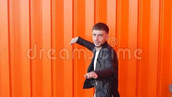 年轻的积极和情绪化的男性深色头发穿着黑色夹克在橙色背景下跳舞特写慢镜头视频的预览图