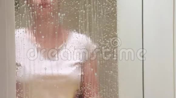 无法辨认的女人戴着黄色橡胶手套用黄色的抹布和泡沫清洁剂清洗浴室镜子视频的预览图