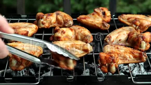 鸡翅烤架人们用金属钳来转动一些辛辣的鸡翅这些鸡翅正在烧烤视频的预览图
