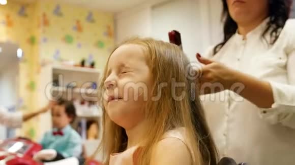 发型师是为小可爱女孩卷发使用电动卷发熨斗背景上的小男孩滑块视频的预览图