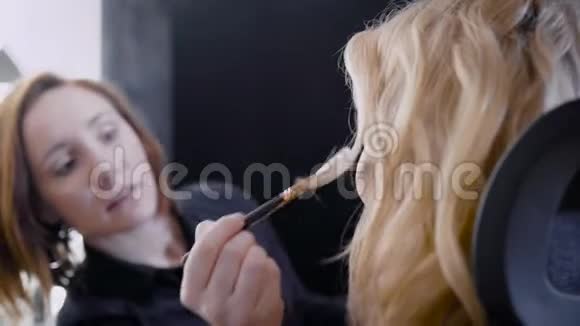侧面拍摄一个迷人的金发女孩在美容院化妆专业服务视频的预览图