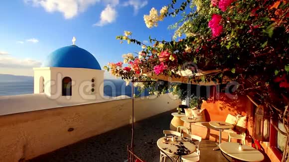 在典型的希腊传统自助餐厅的露台上带风的蓝色教堂圆顶与五颜六色的花灌木嬉戏视频的预览图