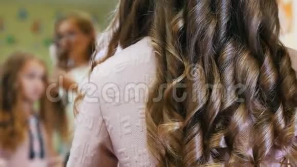 发型师是为小可爱女孩卷发使用电动卷发熨斗对着镜子的背面视频的预览图