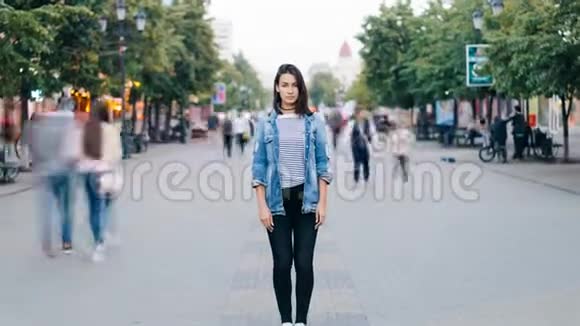 一个穿着时髦服装的漂亮女孩独自看着一个人站在步行街上的摄像机的时间流逝视频的预览图