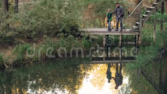 小男孩正在学习从他父亲那里钓鱼他站在木墩上一边说着拿着鱼竿视频的预览图