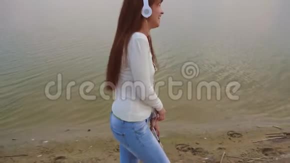 戴着耳机的女孩带着平板电脑去海滩听音乐美丽的女孩笑着笑着视频的预览图