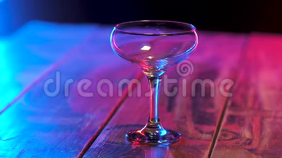 在一个有细茎的杯子里一串红色的酒精鸡尾酒在五彩光中缓慢运动视频的预览图