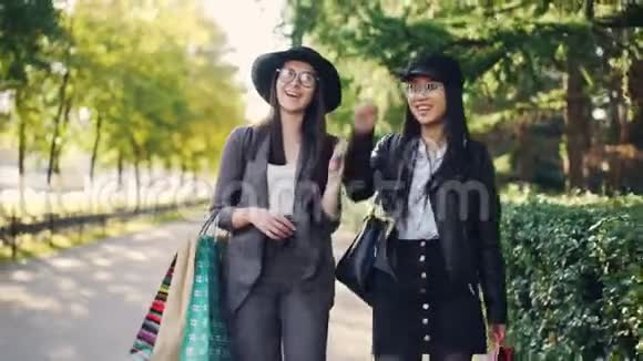 拍摄下来的快乐女千禧一代购物狂和明亮的购物袋一起散步和交谈妇女视频的预览图