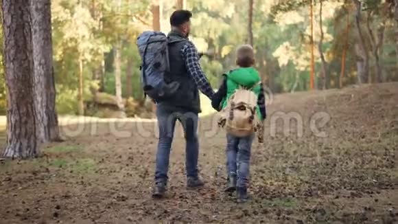 回到幸福的家庭孩子和父亲在森林里散步双手背着背包说话男孩正在投掷视频的预览图
