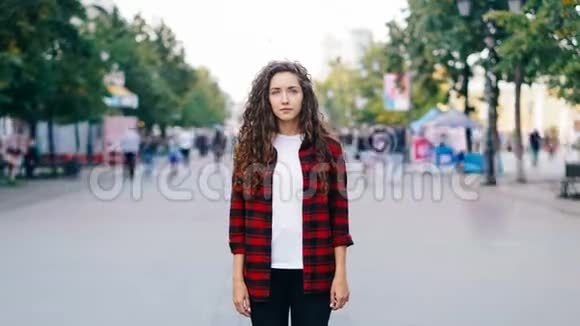 一张严肃的女孩嬉皮士站在市中心的街道上当旁路人在看摄像机时的延时画像视频的预览图