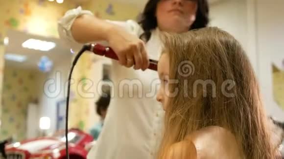 发型师用电卷发熨斗为小可爱的女孩卷发视频的预览图