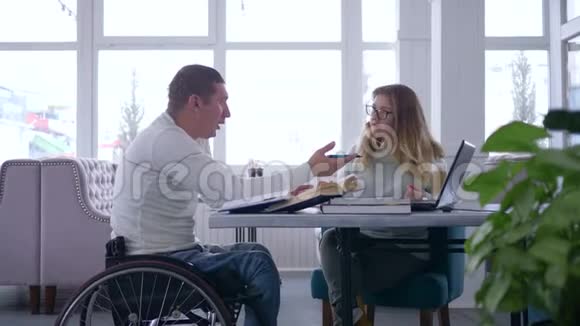 残疾学生个人学习戴眼镜的女教师在轮椅上为残疾男子讲课视频的预览图