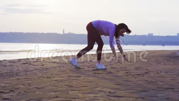 一位留着黑色长发的年轻女子在一条大河的沙岸上做体操视频的预览图